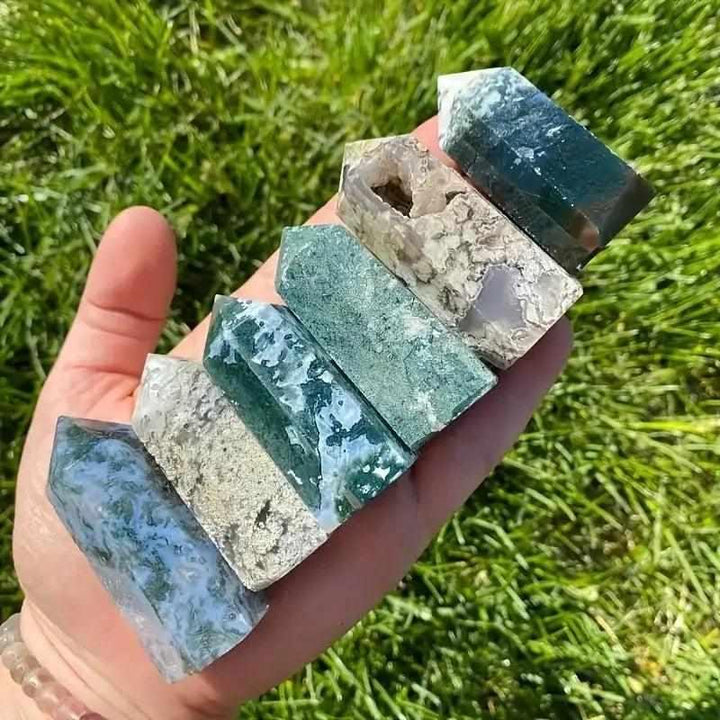 Hand holding five polished Moss Agate hexagonal towers with green moss-like inclusions for heart chakra healing.