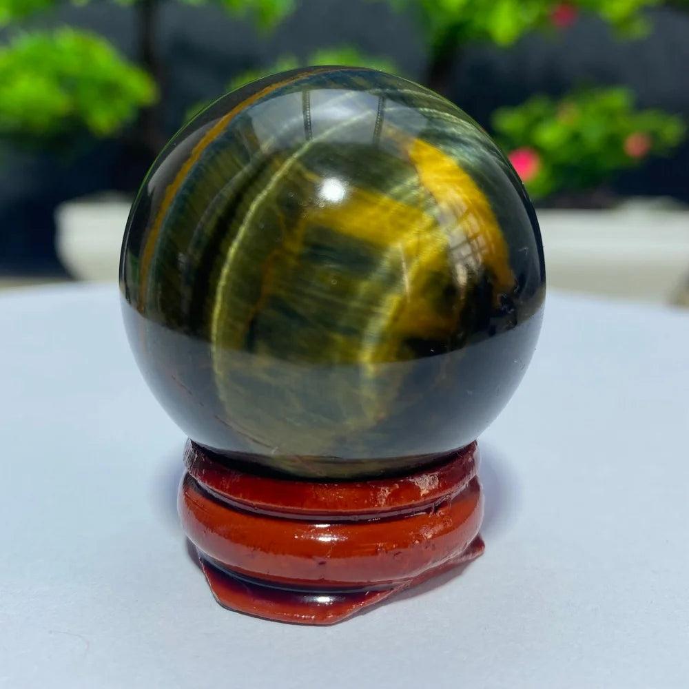 Polished blue and yellow Tiger Eye crystal ball on a wooden stand, perfect for Reiki healing and spiritual home decor.