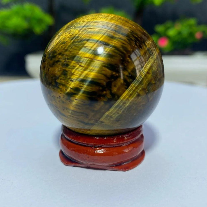Polished yellow Tiger Eye crystal ball on a wooden stand, perfect for Reiki healing, meditation, and spiritual home decor.