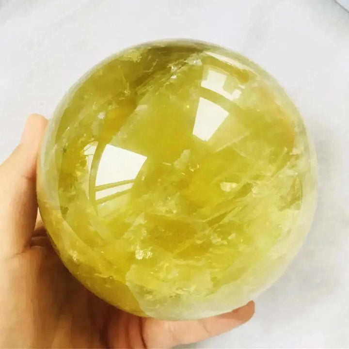 Hand holding a polished, golden-yellow Natural Citrine Quartz Sphere from Crystal Destiny, promoting abundance.