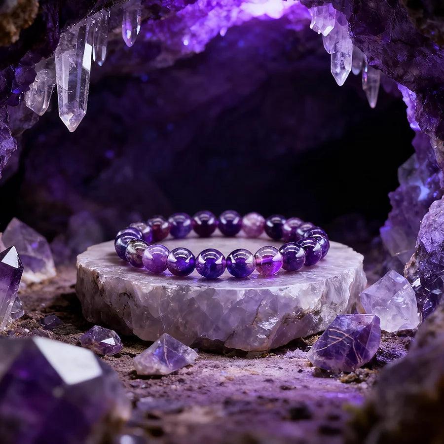 Vibrant purple amethyst bracelet with natural stone beads, displayed on a crystal slab in a mystical cave setting.