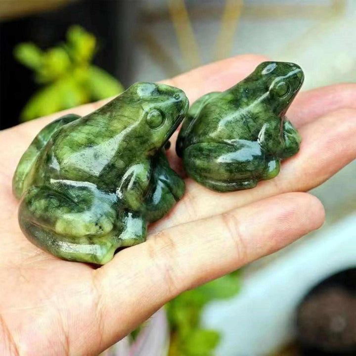 Two vibrant Xiuyan Jade frog figurines, symbolizing abundance and transformation, held in a palm.