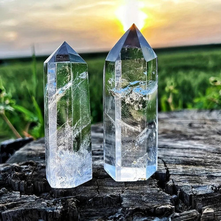 Two natural clear quartz hexagonal obelisk wands with transparent, healing energy set against a sunset landscape.