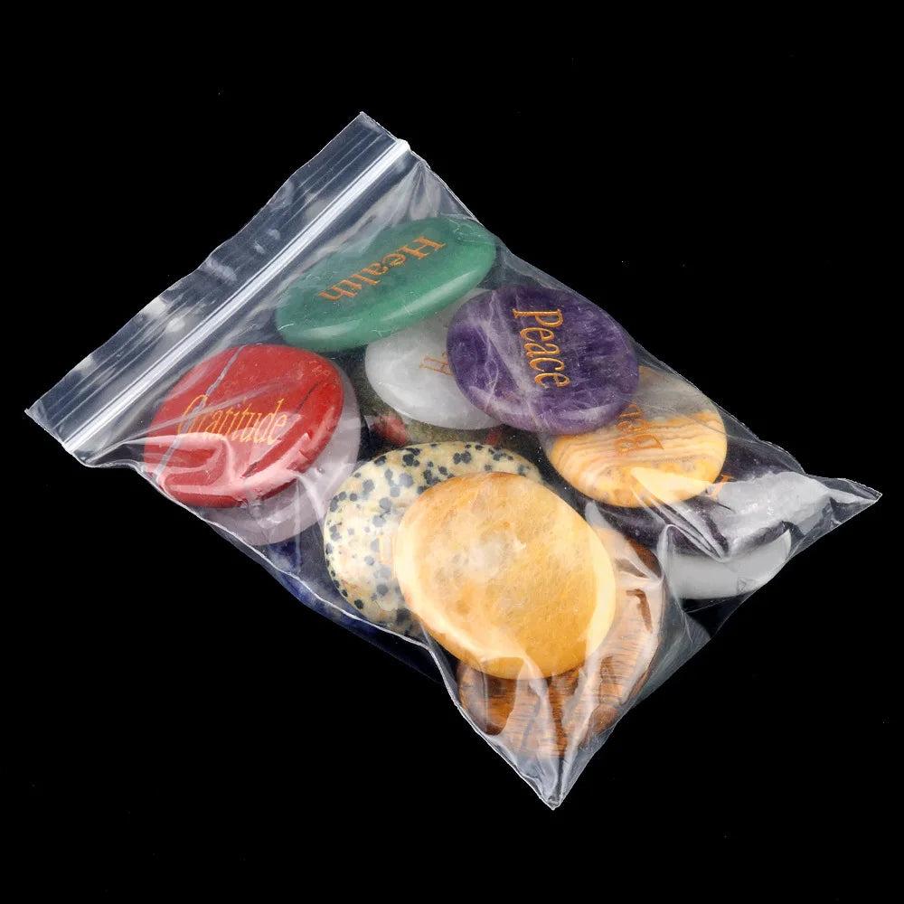 Assorted natural crystal oval palm stones with gold-filled engraved inspirational words like "Peace" and "Health," packaged for serenity.