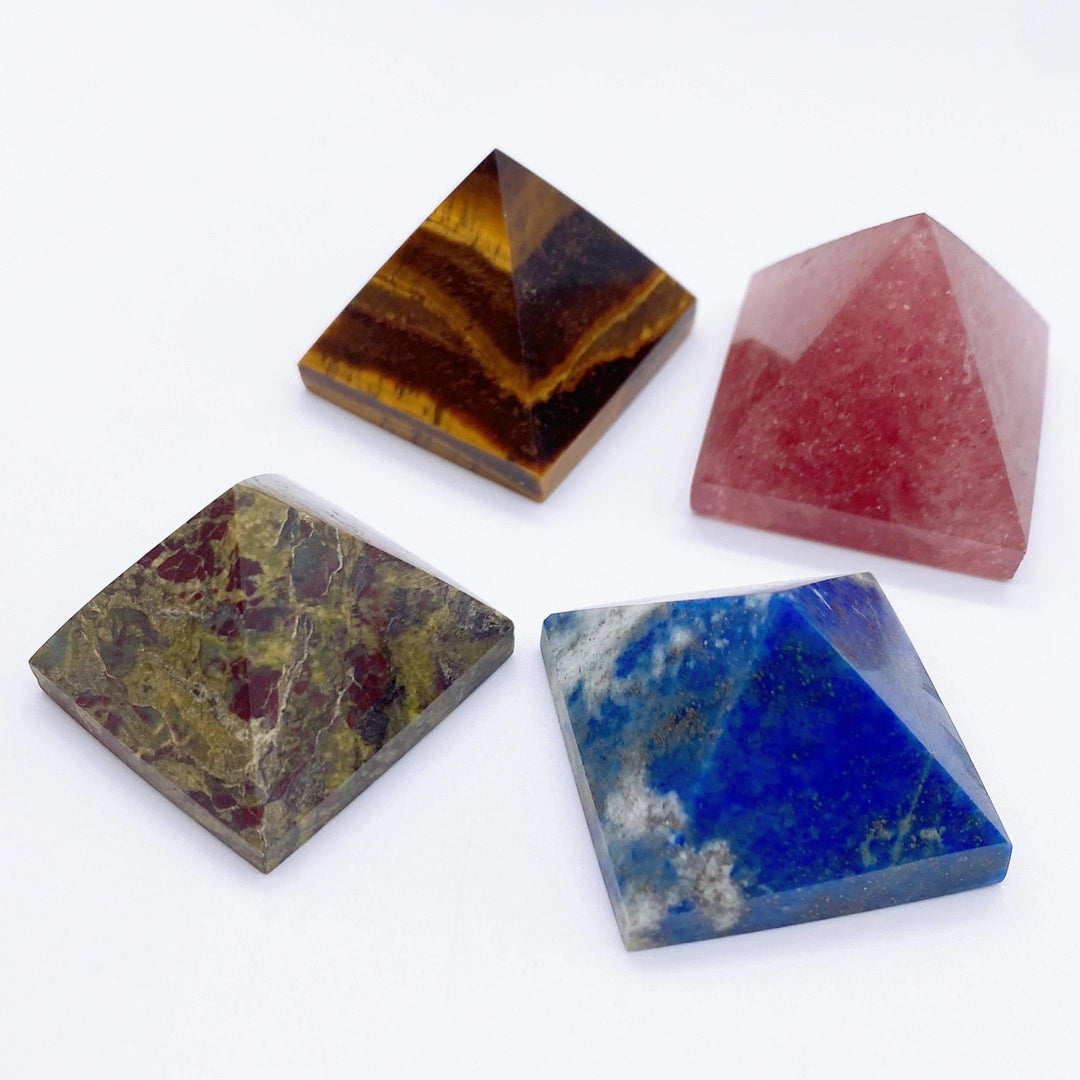 Four polished crystal pyramids: golden-brown Tiger Eye, deep red Strawberry Quartz, green and red Dragon Blood Stone, and blue Lapis Lazuli.