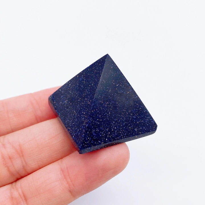 Hand holding a sparkling blue goldstone pyramid, a healing crystal for energy and meditation.