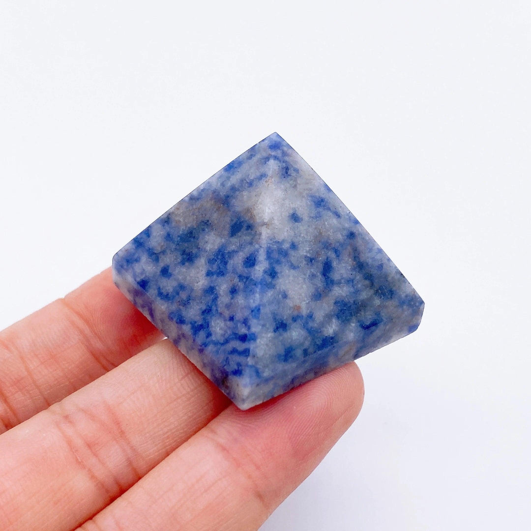 Hand holding a small, deep blue Sodalite crystal pyramid with white and grey flecks.