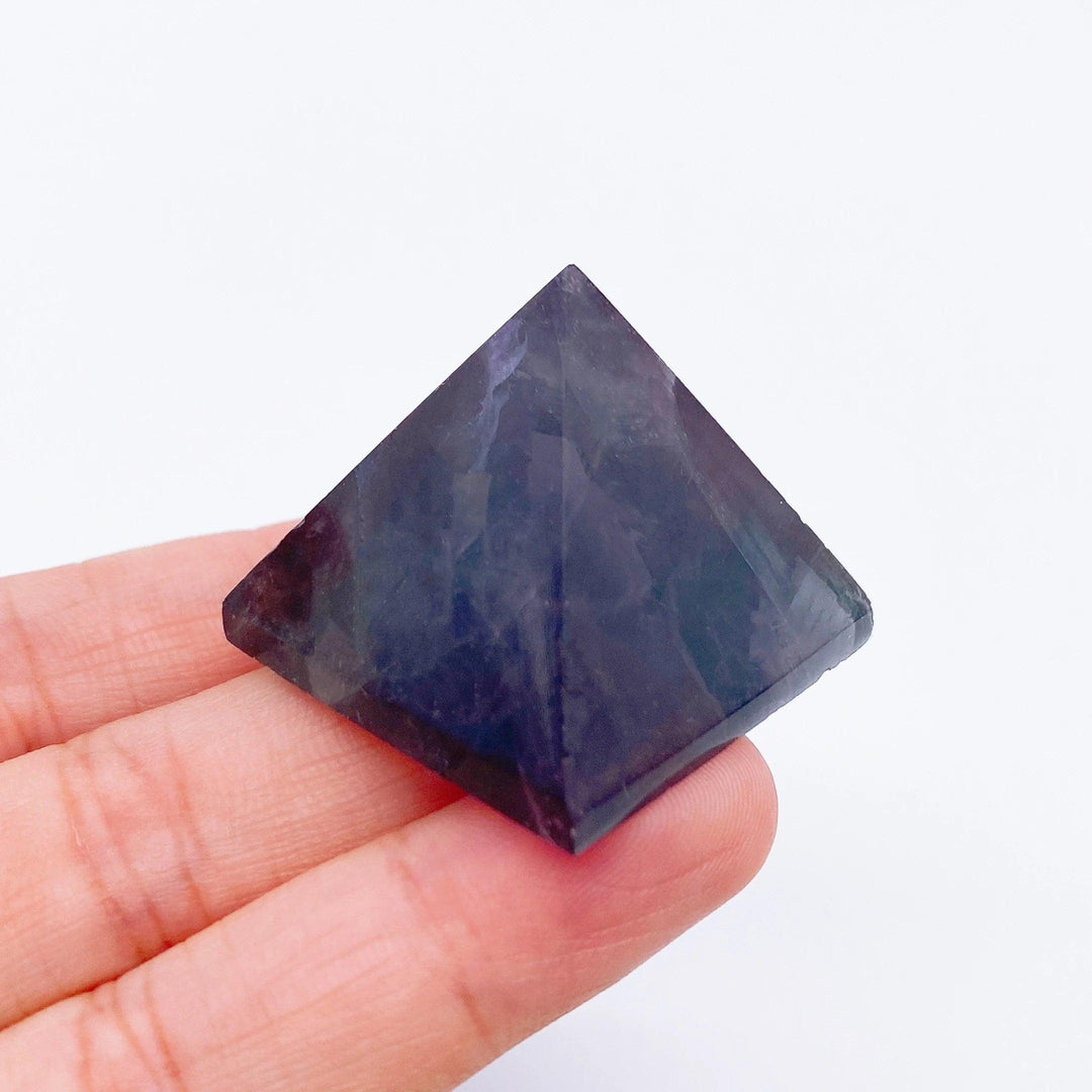 Hand holding a small, dark purple Fluorite crystal pyramid, ideal for healing and meditation.