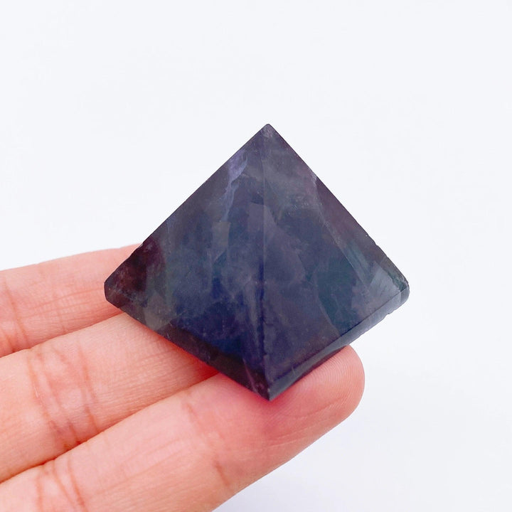 Hand holding a small, dark purple Fluorite crystal pyramid, ideal for healing and meditation.