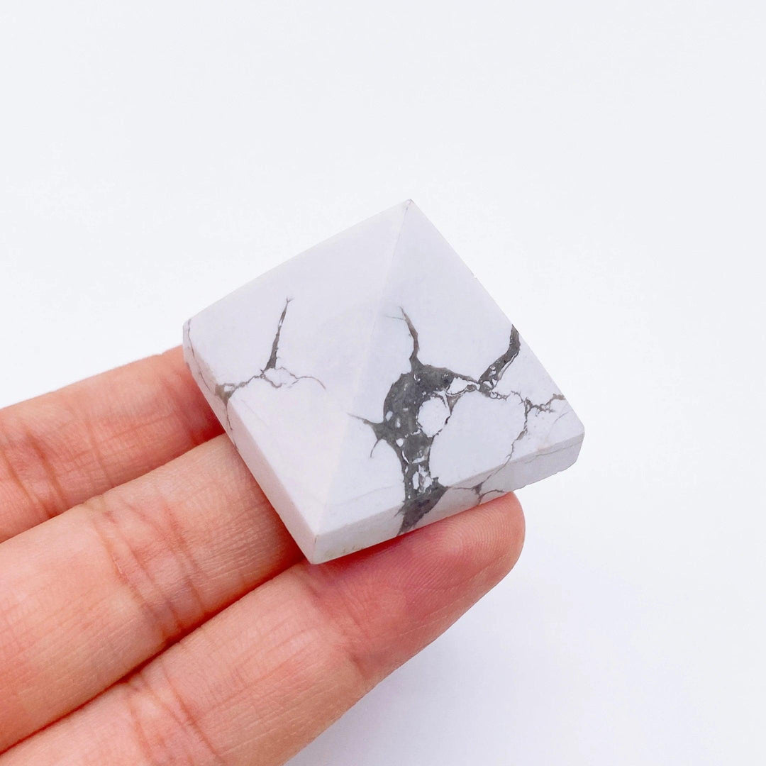 Hand holding a small white Howlite crystal pyramid with natural gray veins, ideal for healing.