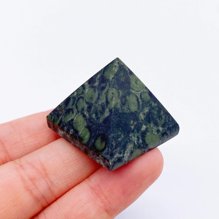 Kambaba Jasper crystal pyramid, dark green with black spots, held in hand. Healing stone.