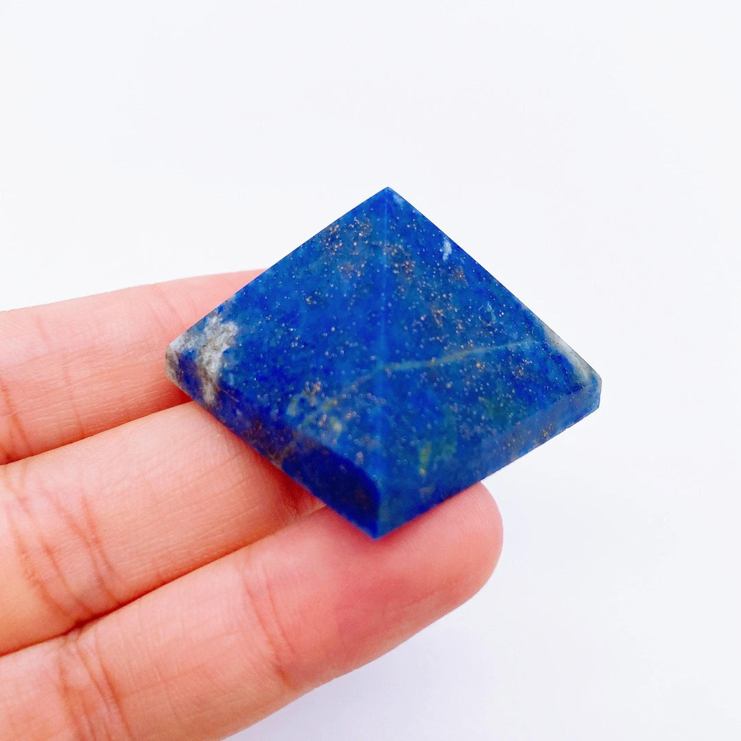 Hand holding a small, deep blue Lapis Lazuli crystal pyramid with gold flecks, ideal for healing and meditation.