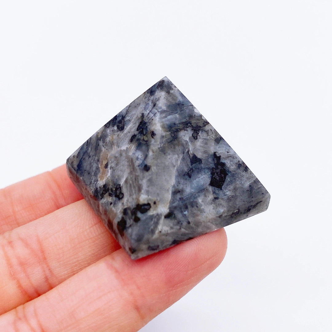 Hand holding a small, dark gray and black speckled Yooperlite crystal pyramid, ideal for healing.