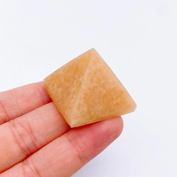 Hand holding a small, smooth orange aventurine crystal pyramid, ideal for healing and meditation.
