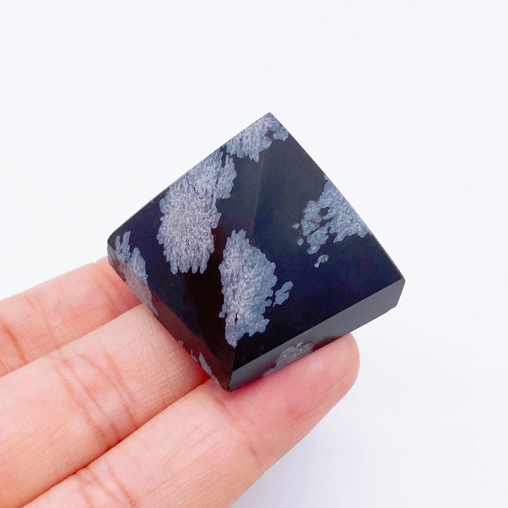 Hand holding a black Snowflake Obsidian crystal pyramid with white snowflake patterns, ideal for healing.