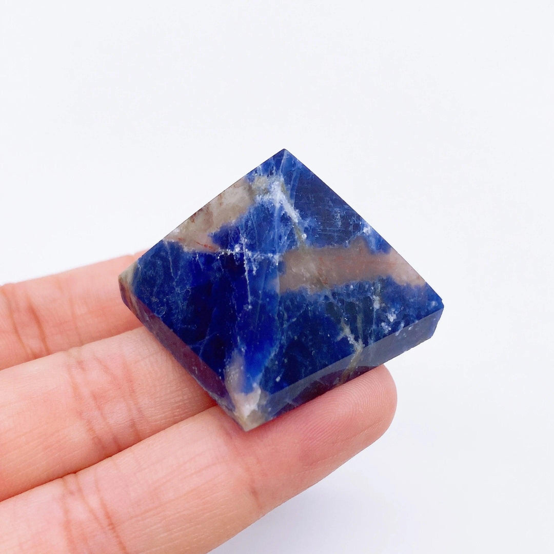 Hand holding a deep blue Sodalite crystal pyramid with white and brown veins, 30mm, for healing.