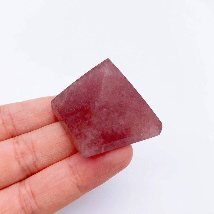 Hand holding a small, vibrant red Strawberry Quartz crystal pyramid, ideal for healing and meditation.