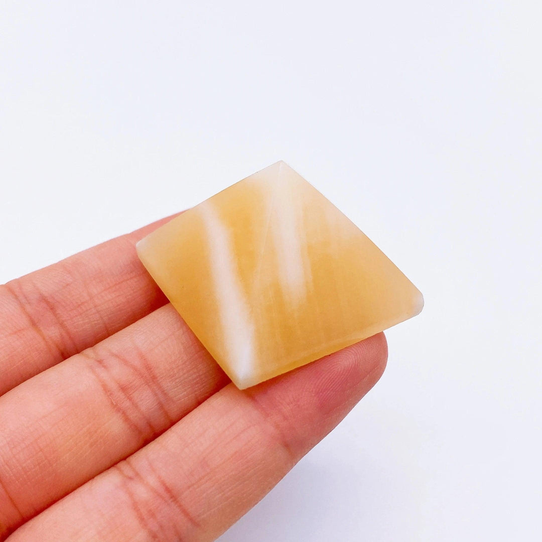 Hand holding a 30mm yellow calcite crystal pyramid with white stripes, ideal for healing and meditation.