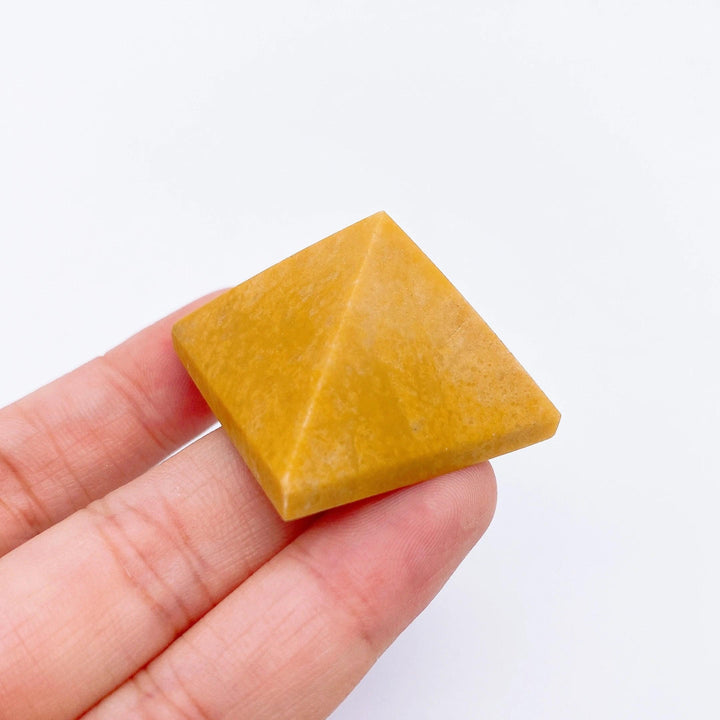 Hand holding a small, golden yellow calcite crystal pyramid, ideal for healing and meditation.
