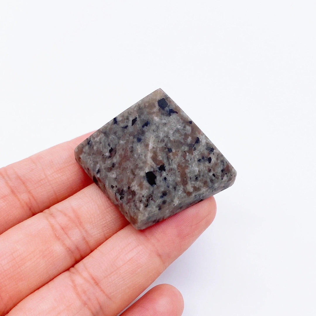 Hand holding a small, speckled gray Yooperlite crystal pyramid, ideal for healing and meditation.