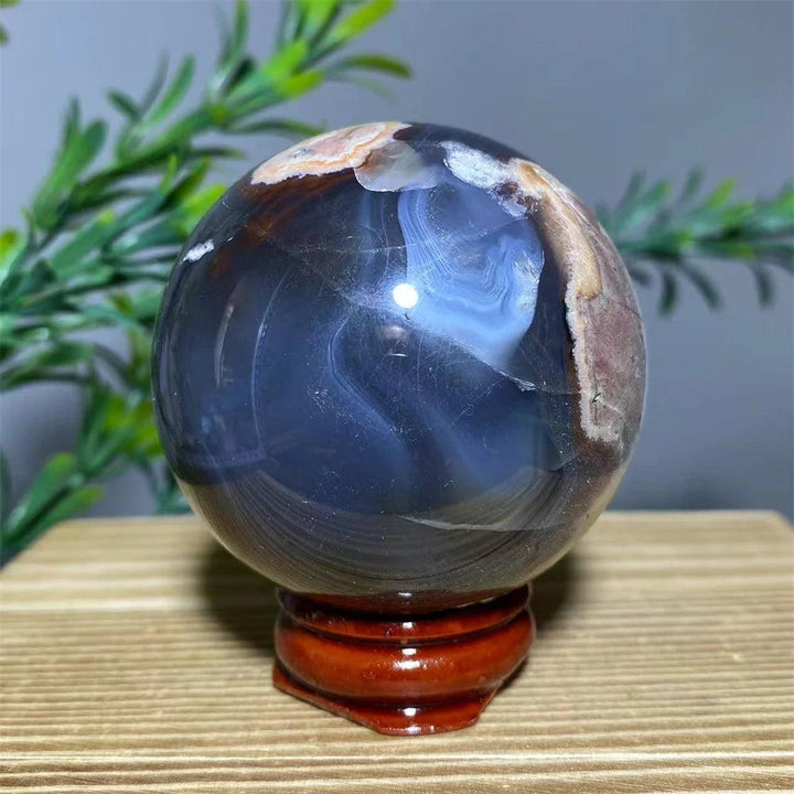 Natural dark blue and brown agate sphere with white flash, on a wooden stand, for spiritual decoration.