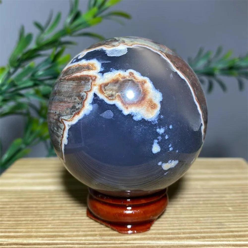 Natural agate sphere with dark blue, white, and brown patterns, displayed on a wooden stand.