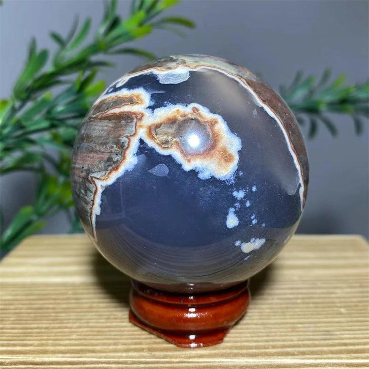 Natural agate sphere with dark blue, white, and brown patterns, displayed on a wooden stand.