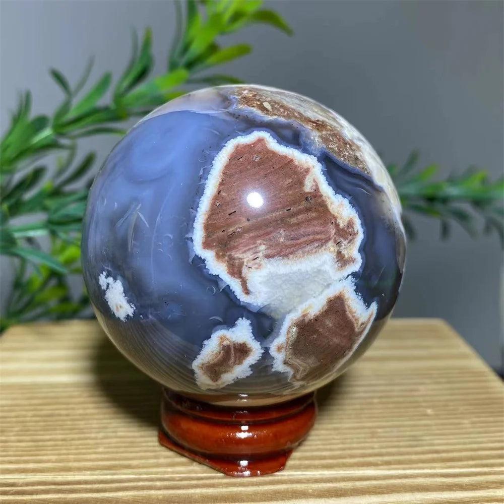 Natural agate sphere with blue, brown, and white patterns on a wooden stand, promoting spiritual healing.