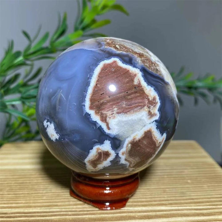 Natural agate sphere with blue, brown, and white patterns on a wooden stand, promoting spiritual healing.