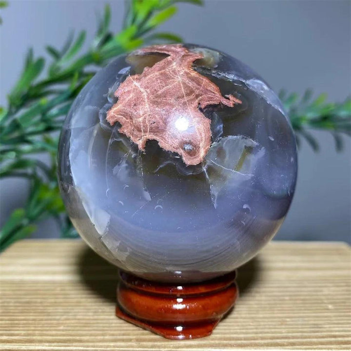 Natural agate sphere with unique reddish-brown inclusions, on a wooden stand.