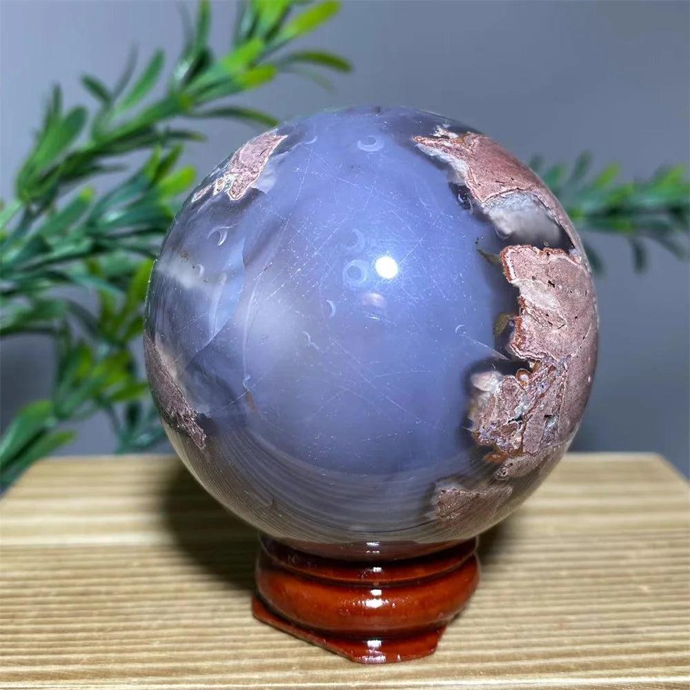 Natural purple agate sphere with brown and white inclusions on a wooden stand.