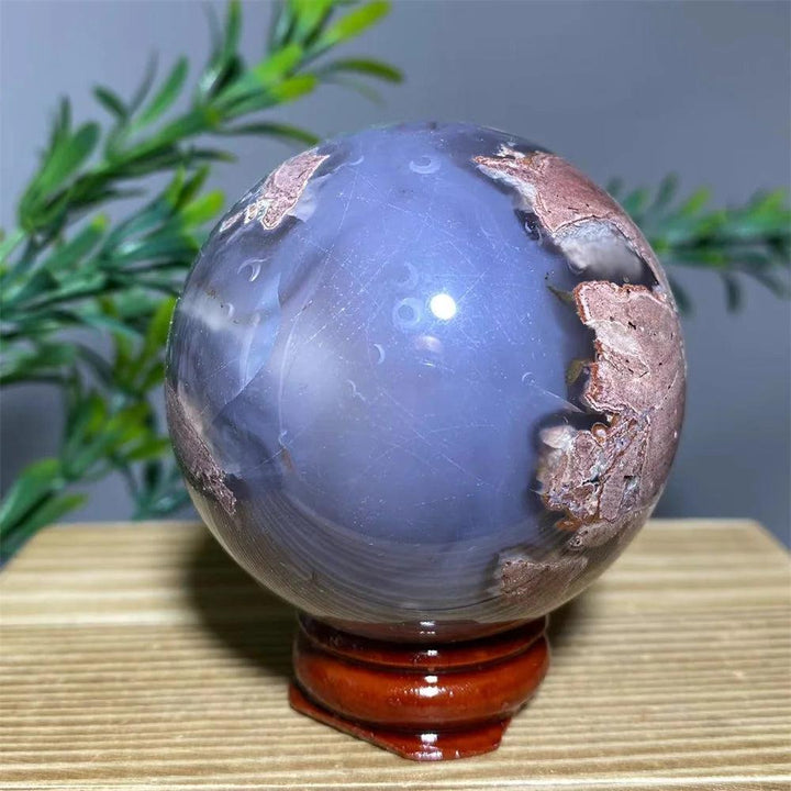 Natural purple agate sphere with brown and white inclusions on a wooden stand.
