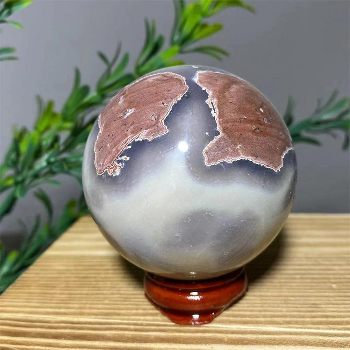 Natural Crystal Football Agate Sphere with unique brown and white patterns, on a wooden stand.