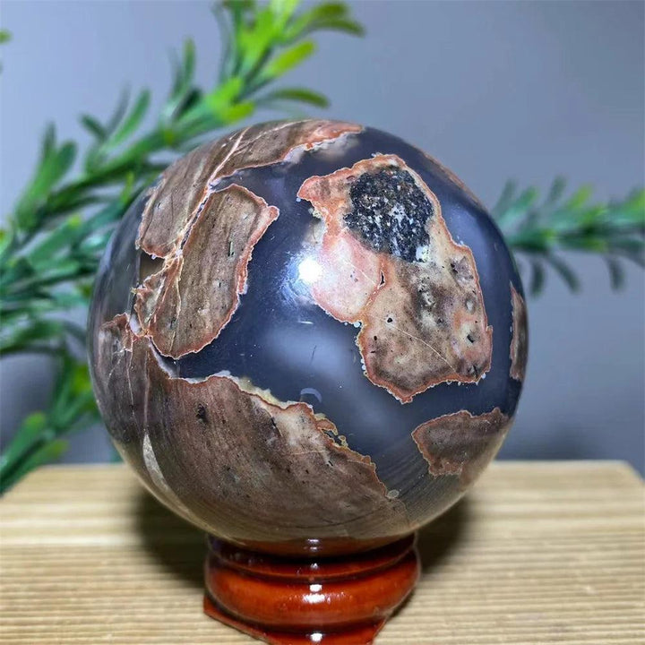 Natural agate sphere with brown, black, and gray patterns on a wooden stand, promoting spiritual healing.