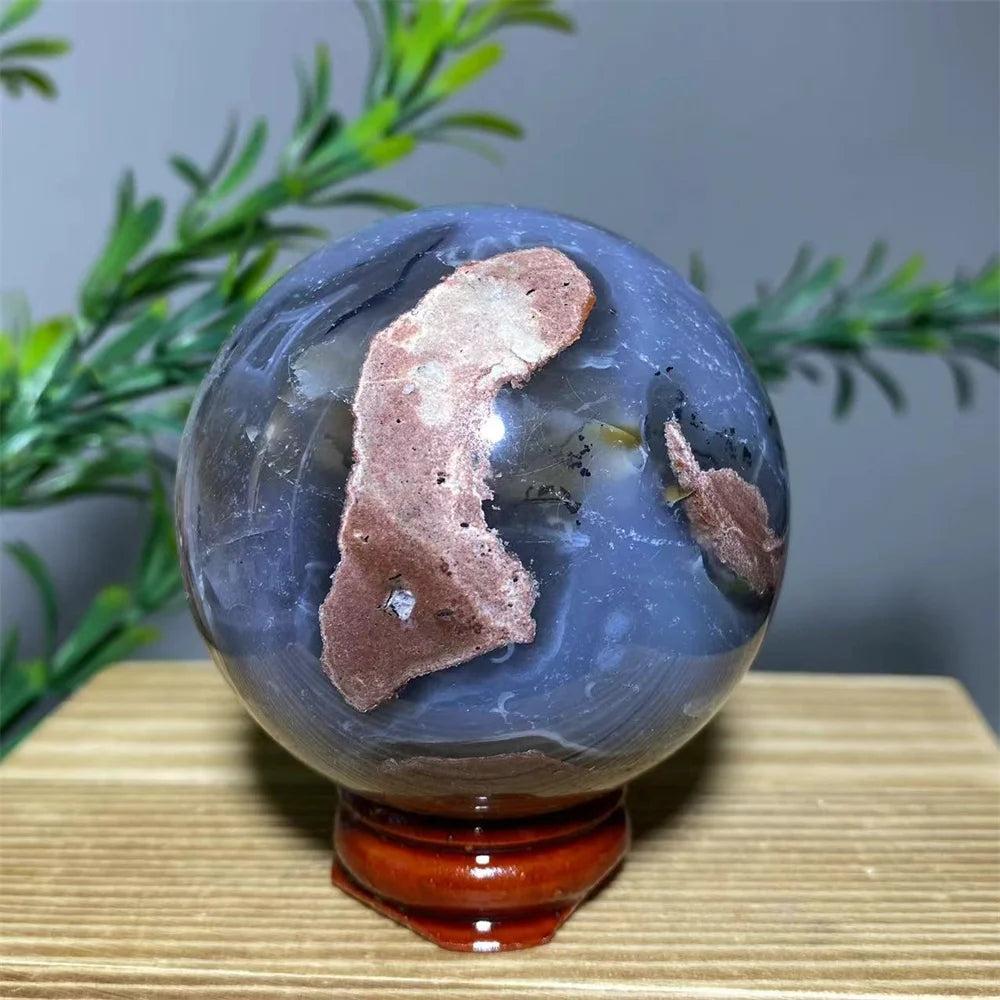 Natural blue and brown agate sphere with flash stone quartz, displayed on a wooden stand.