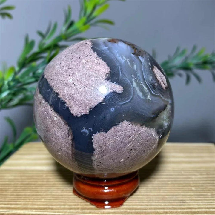 Natural crystal football agate sphere with brown and grey patterns on a wooden stand.