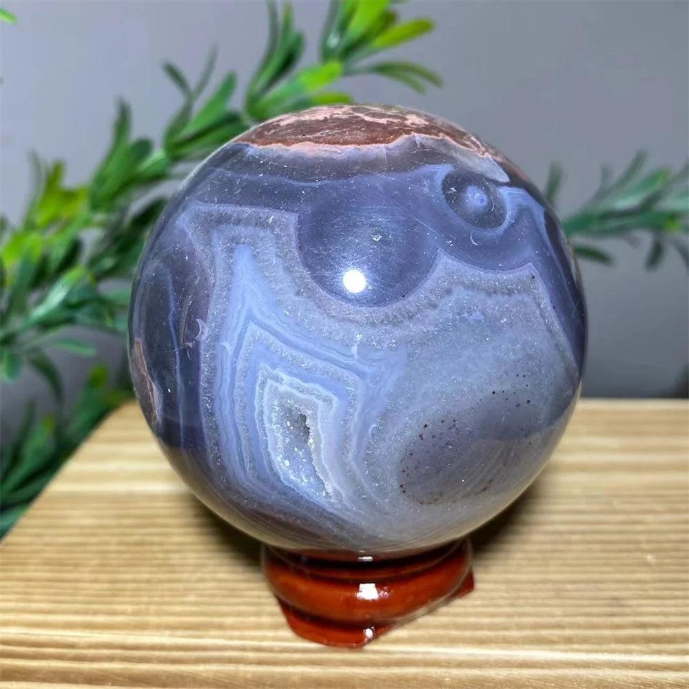 Natural blue and purple agate sphere with white crystal geode details on a wooden stand.