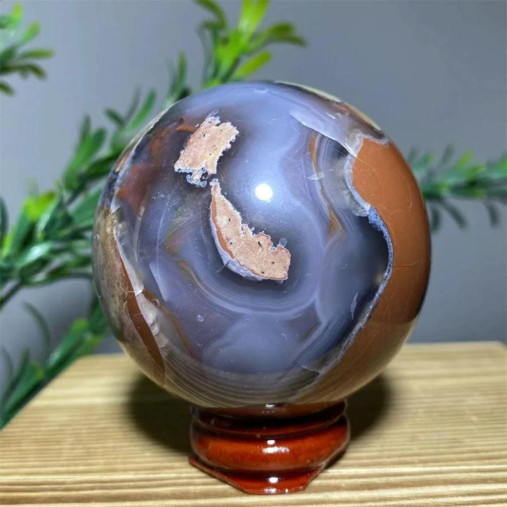Natural agate sphere with swirling blue, brown, and white patterns on a wooden stand, promoting spiritual healing.