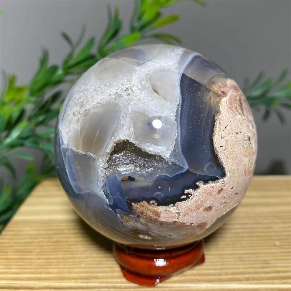Natural crystal agate sphere with white geode interior, blue-grey bands, and earthy pink tones on a wooden stand.