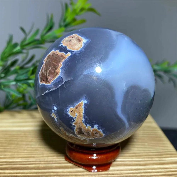 Natural gray agate sphere with brown inclusions on a wooden stand, promoting spiritual healing.