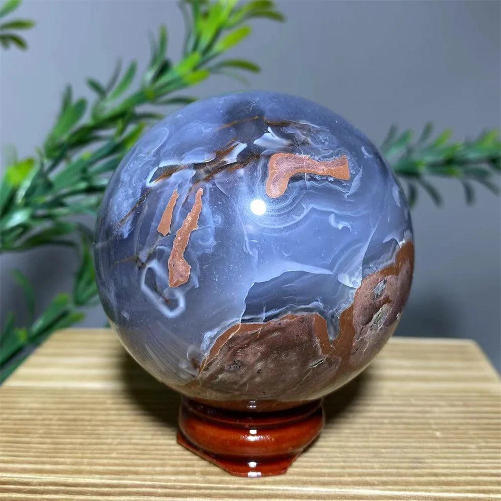 Natural agate sphere with blue, white, and earthy brown patterns on a wooden stand, ideal for home decor.