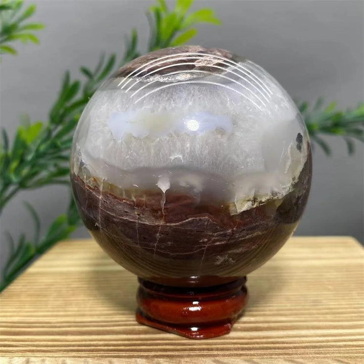 Natural agate sphere with white, brown, and grey bands on a wooden stand, ideal for home decor.