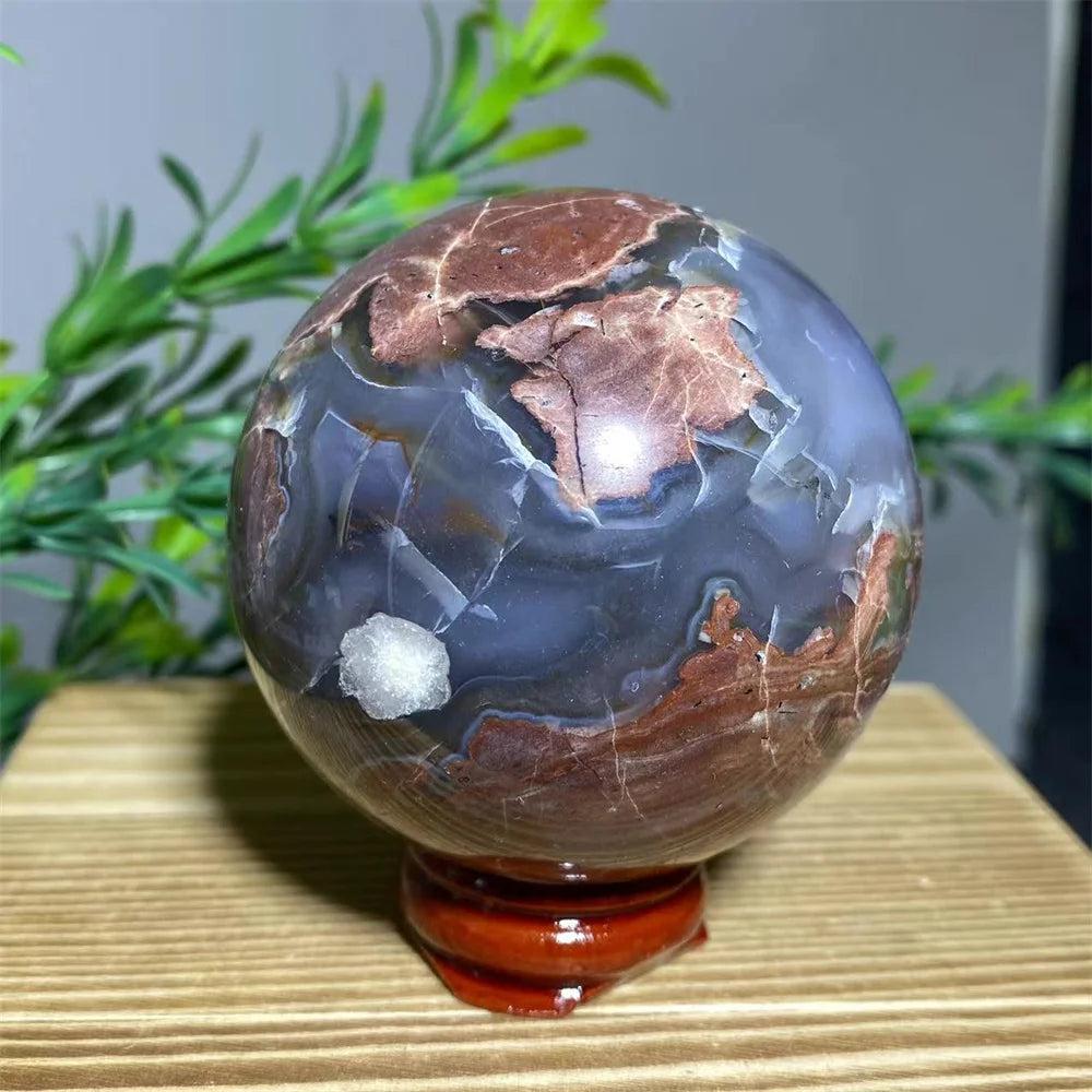 Natural crystal football agate sphere with earthy red and blue-grey patterns on a wooden stand.