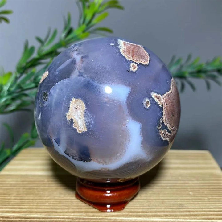 Natural purple agate sphere with brown and white inclusions on a wooden stand.