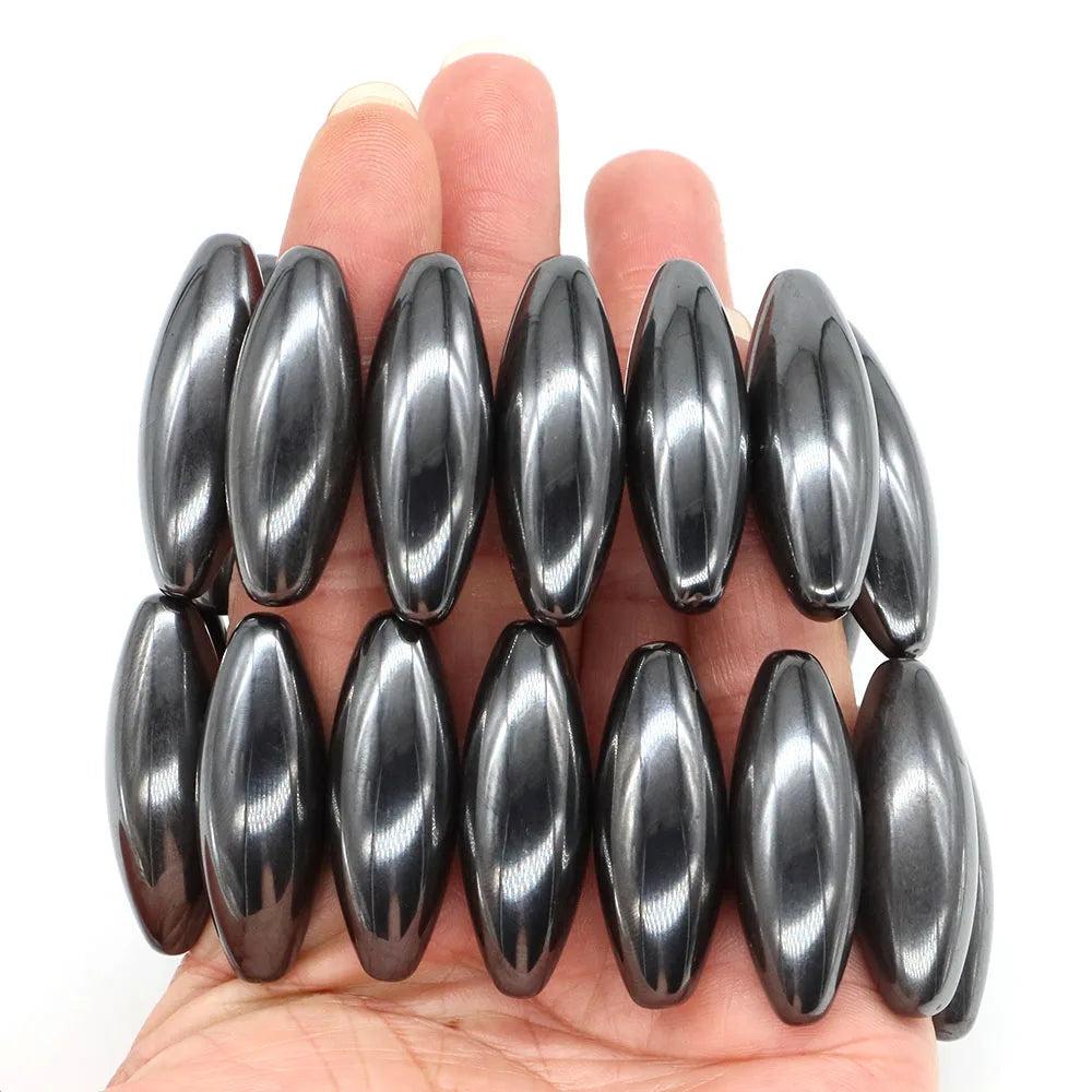 Hand holding twelve dark grey, metallic, olive-shaped natural magnetic hematite beads, 38x13mm, for grounding.