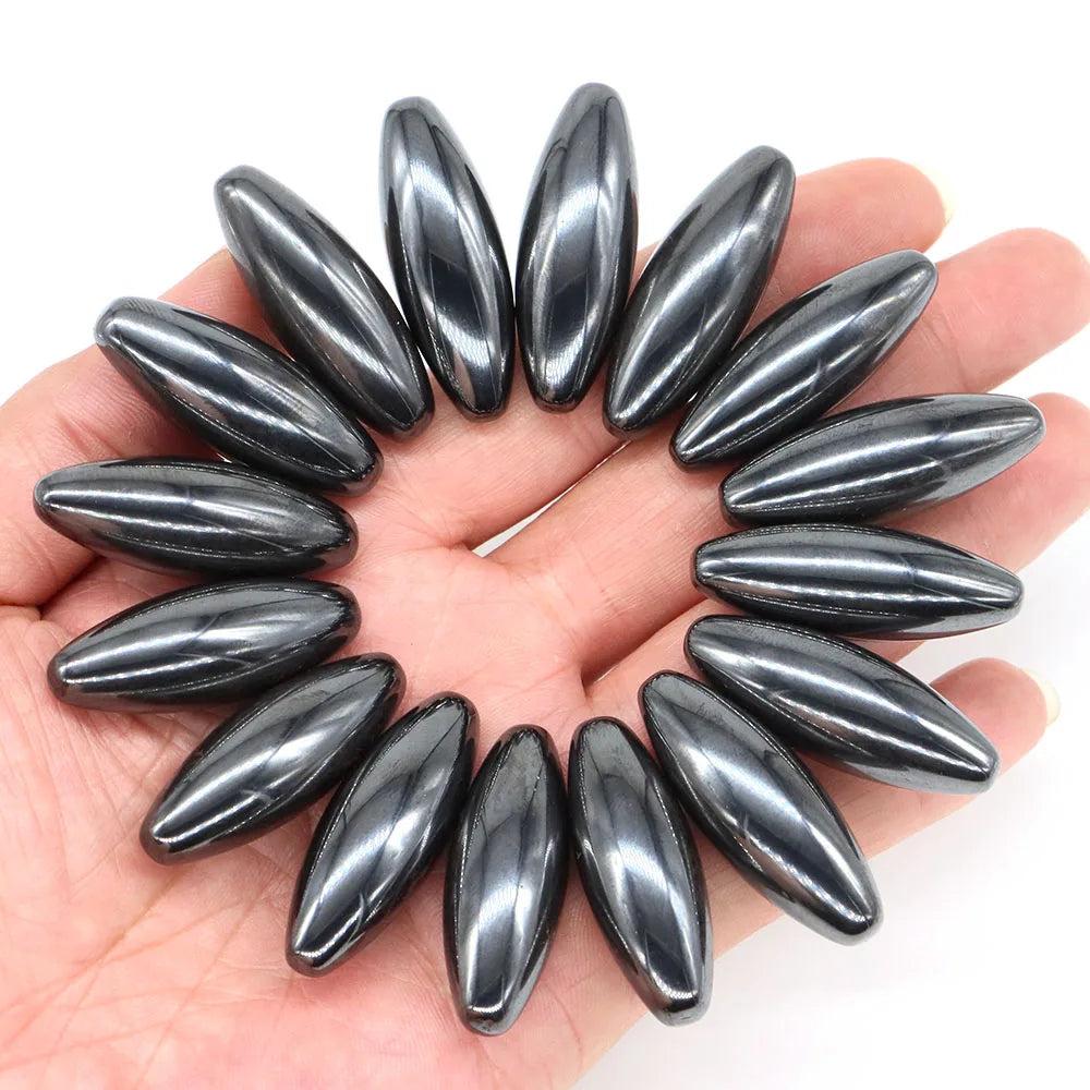 Polished, dark gray magnetic hematite olive-shaped beads, 38x13mm, arranged in a circle on a hand.
