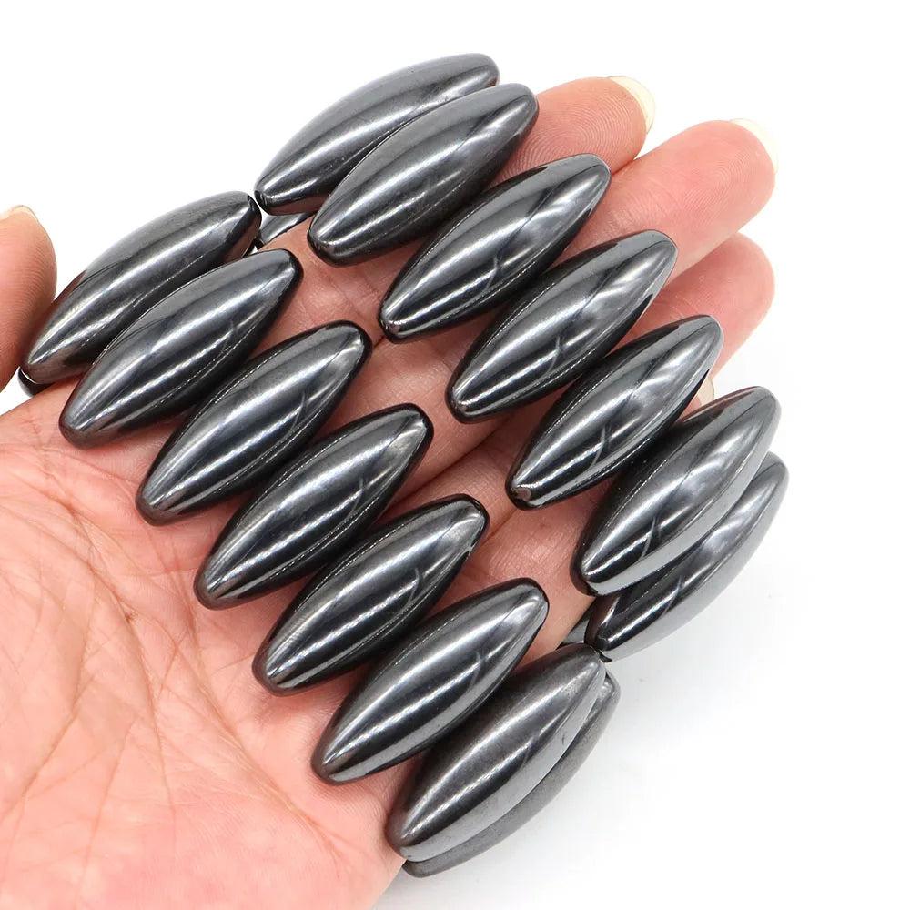 Polished, dark gray magnetic hematite olive-shaped beads, 38x13mm, held in a hand, for grounding and stability.