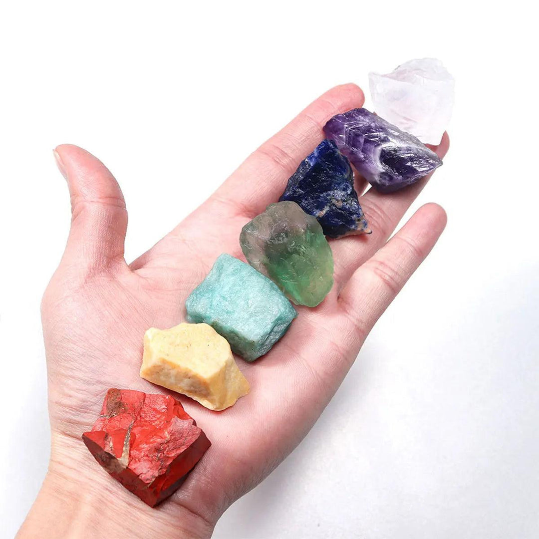 Hand holding 7 raw chakra healing crystals, including red jasper and amethyst, for natural energy and spiritual balance.