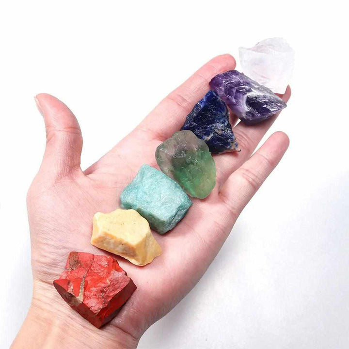 Hand holding 7 raw chakra healing crystals, including red jasper and amethyst, for natural energy and spiritual balance.