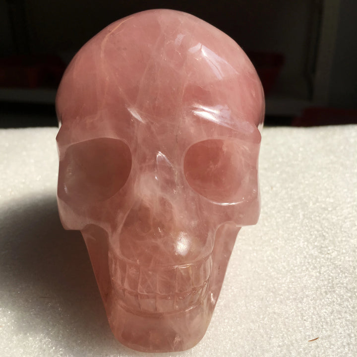 Hand-carved natural rose quartz crystal skull for Reiki healing, featuring a smooth, polished pink stone design.